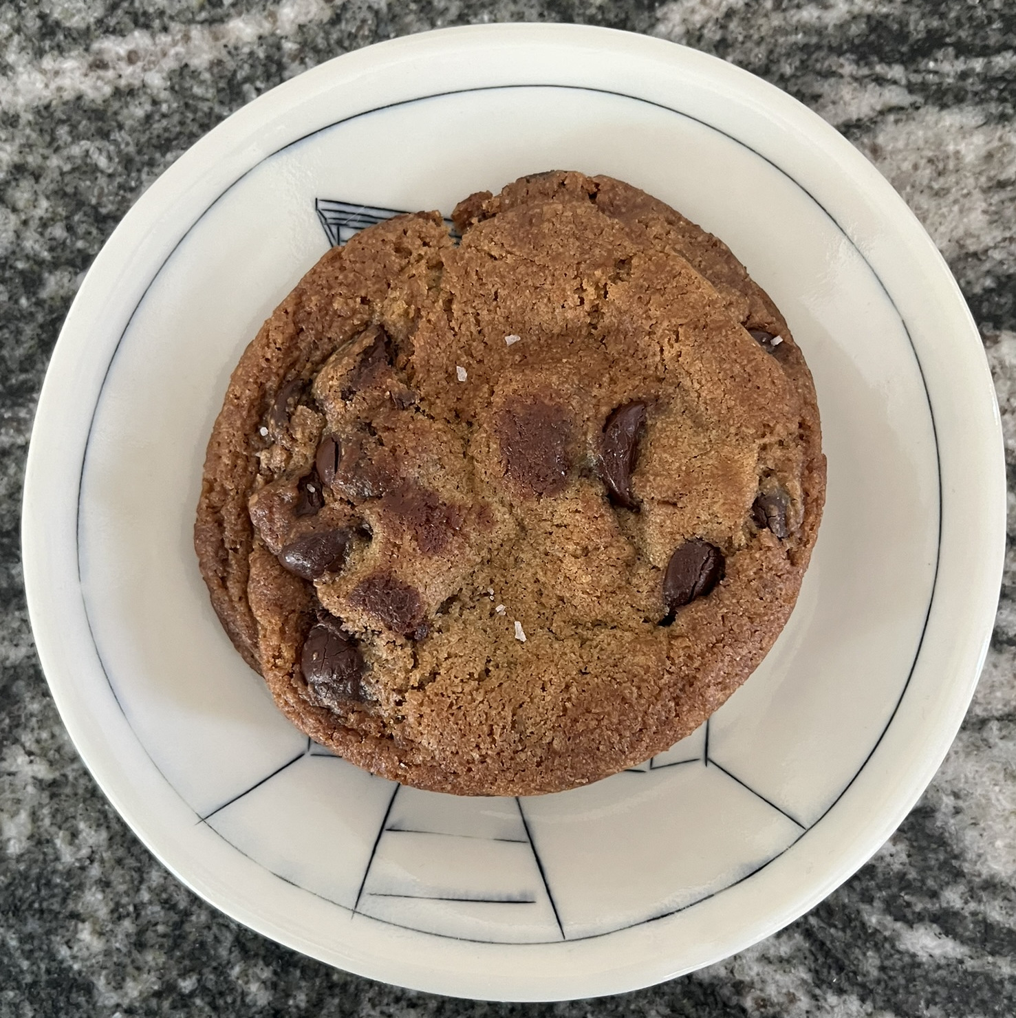 A perfectly round cookie with some chocolate poking through and salty flakes on top