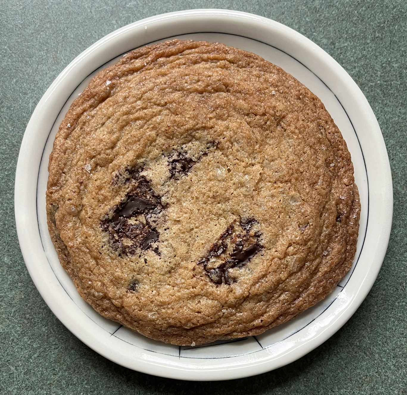 A large diameter cookie with pools of chocolate poking out, salty flakes, and rippled edges